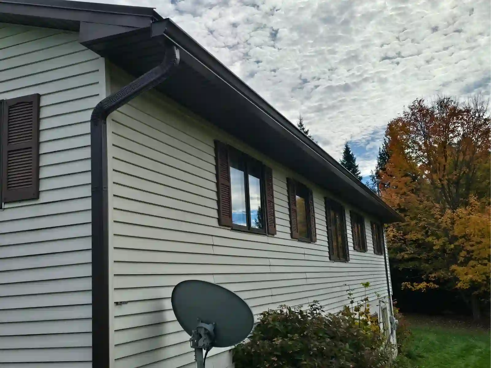 Brown seamless gutters on a two-story home with fall trees behind