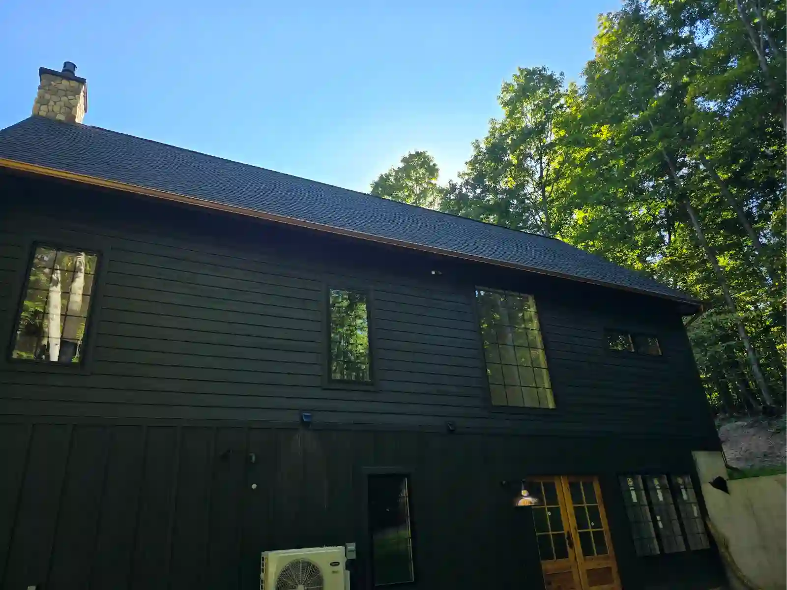 Dark home with new gutters and guards in a wooded yard