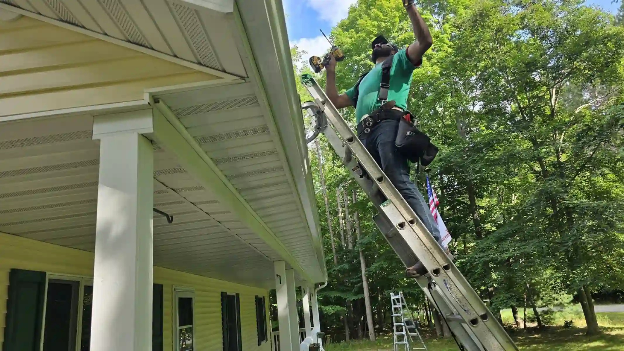 Crew member on a ladder working on a gutter under a porch roof