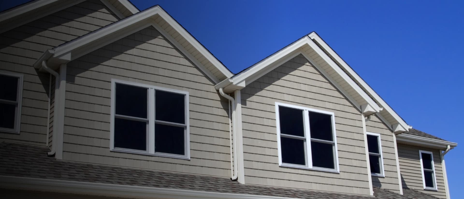 Gray-sided home with white seamless gutters against a deep blue sky